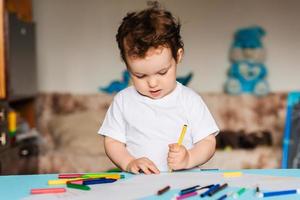 um menino bonitinho desenha em seu caderno de desenho com lápis de cor foto