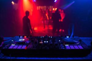 console de dj para mixagem de música com pessoas embaçadas dançando em uma festa de boate foto