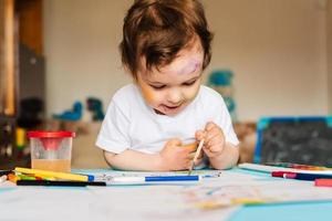 criança alegre feliz desenhando com pincel no álbum usando muitas ferramentas de pintura. foto