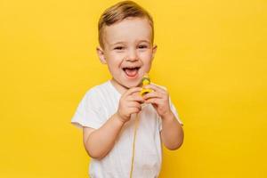 retrato de um menino rindo bonito em um fundo amarelo com um brinquedo nas mãos. copie o espaço. foto