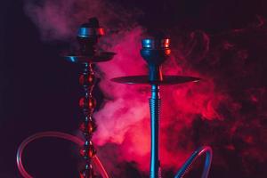 tigela de cachimbo de água, shisha e carvões em um fundo preto esfumaçado com iluminação colorida foto