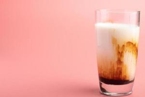 leite de açúcar mascavo fresco em um copo transparente no fundo rosa foto
