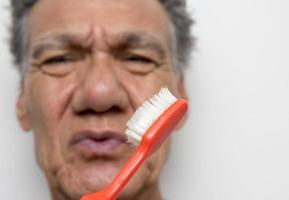 homem sênior olhando para sua velha e desgastada escova de dentes foto