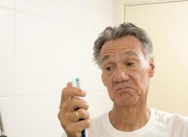 homem sênior olhando para sua velha e desgastada escova de dentes foto