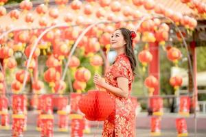 feliz Ano Novo Chinês. mulher asiática usando vestido cheongsam qipao tradicional parecendo confiante segurando lanterna enquanto visitava o templo budista chinês foto