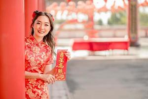 feliz Ano Novo Chinês. mulher asiática usando vestido cheongsam qipao tradicional segurando cartão de fortuna de bênção no templo budista chinês. texto chinês significa abençoado por uma estrela da sorte. sorriso de emoção foto