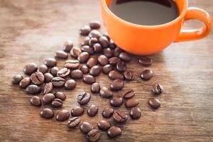 grãos de café com uma xícara de café em uma mesa de madeira foto