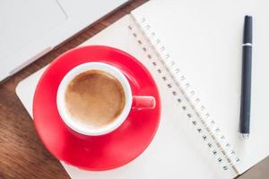 vista superior de uma xícara de café vermelha e caneta em um caderno foto