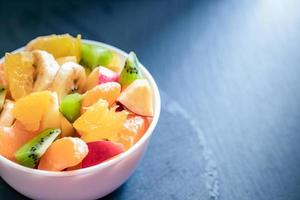 copo branco iluminado com salada de frutas frescas em fundo cinza escuro. foto