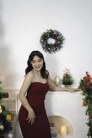 retrato de uma jovem bonita vestindo um vestido vermelho, sorrindo para a câmera, de pé na sala de natal decorada dentro de casa foto