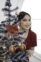 retrato de uma linda jovem decorando a árvore de natal, sorrindo usando vestido vermelho na sala de natal decorada dentro de casa foto