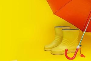 botas amarelas sob um guarda-chuva vermelho sobre um fundo amarelo com espaço de cópia. foto