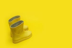 botas de borracha infantil amarelas em um fundo amarelo com espaço de cópia foto