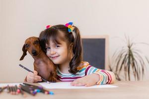 menina bonitinha desenha com seu amigo cachorro dachshund. crianças e animais. cão amigável. foto de alta qualidade