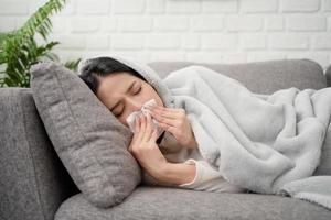 mulher espirrando no sofá na temporada de inverno. ela estava coberta no sofá, sofrendo de gripe. conceito de frio e febre foto