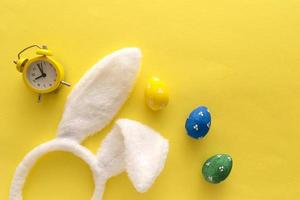 ovos de páscoa decorados e orelhas de coelho na cor de fundo amarelo, vista superior foto