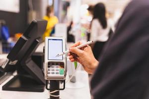 mulheres do consumidor assinando em uma tela sensível ao toque da máquina de transação de cartão de crédito no mercado de jantar. foto