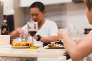 casal jantando com copos de vinho tinto na mesa em casa. foto