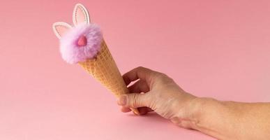 fundo rosa abstrato. uma mão com um coelho lilás fofo em um cone de waffle. o conceito de amor, um cartão para dia dos namorados e páscoa foto
