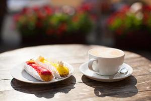 uma caneca de café na mesa e um delicioso eclair em um prato foto