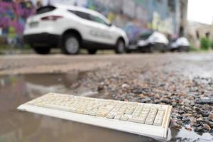 velho teclado de computador quebrado, jogado no lixo deitado na estrada em uma poça. foto