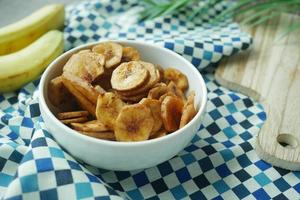 chips de banana seca em uma tigela sobre fundo de azulejos pretos foto