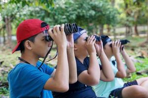 três meninos asiáticos usam binóculos para observar pássaros em uma floresta comunitária própria. o conceito de aprendizagem a partir de fontes de aprendizagem fora da escola. foco no primeiro filho.