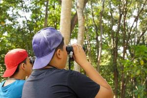 meninos asiáticos usam binóculos para observar pássaros em uma floresta comunitária própria. o conceito de aprendizagem a partir de fontes de aprendizagem fora da escola. foco suave e seletivo. foto