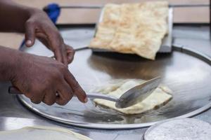 mão segurando uma espátula, fritando o roti em uma panela com óleo fervente. foto