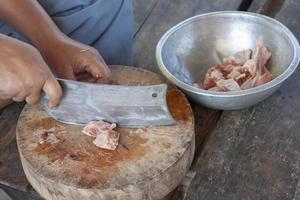 a mão do cozinheiro segura a faca cortando frango em uma tábua de madeira para cozinhar em uma cozinha campestre. foto