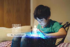 conceito de aprendizado de tecnologia educacional, garoto usando bot de bate-papo construindo jogo de robô em tablet com ícone de rosto de notificação pop-up, robô de programação de menino com tela de exposição, navegação na web, interface de diagrama cibernético foto