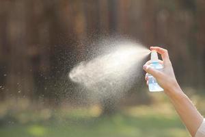 mão de uma mulher segurando uma garrafa e pulverizando no fundo da natureza. anti-séptico, repelente de mosquitos, refrescando o ar foto