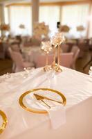 decoração de mesa com toalha de mesa rosa, castiçais de cristal com velas e flores rosa brancas no restaurante. dia de casamento elegante. mesa de ajuste com placa de ouro, garfo e faca foto