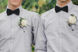 flores de rosas brancas na botoeira, dois noivos amigos estão vestidos com uma camisa cinza e uma gravata borboleta. dia do casamento. look do dia. foto