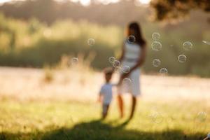 pai, mãe e filho sopram bolhas de sabão no parque juntos em um dia ensolarado de verão. família feliz se divertindo ao ar livre. foco seletivo foto