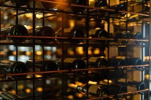 muitas garrafas de vinho de vidro em prateleiras de vinho com iluminação. interior do restaurante. foto colorida