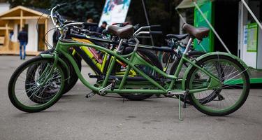 uma bicicleta tandem de cor verde com rodas escarlates está estacionada em um estacionamento perto da ciclovia foto
