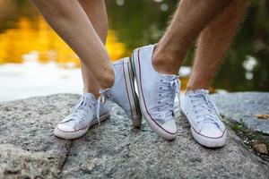 história de amor contada por botas. pés humanos de perto. homem e mulher de tênis. garota de sapatos brancos. cara de tênis preto e jeans. casal moderno no verão. as pernas fecham. foto