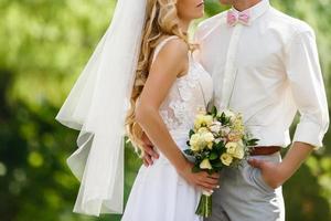 Casamento. o noivo de terno e a noiva de vestido branco, lado a lado, segurando buquês de flores brancas e folhagens foto