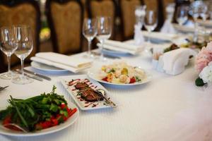 servido para uma mesa de banquete. taças de vinho com guardanapos, copos e saladas. foto