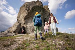 crianças explorando a natureza. as crianças usam mochila caminhando com a mãe perto de uma grande pedra na colina. pidkamin, Ucrânia. foto