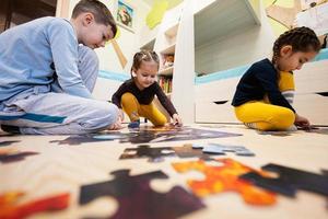 crianças conectando peças de quebra-cabeça em um quarto infantil no chão de casa. diversão em família atividade lazer. foto