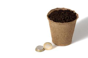 moeda e um pote de turfa para mudas deitados juntos, em uma empresa de produção agrícola rural isolada sobre o branco. foto