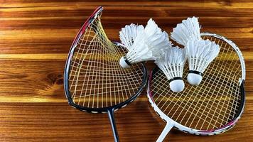 close-up de raquetes de badminton quebradas e galos de peteca de badminton branco sobre fundo de madeira marrom foto