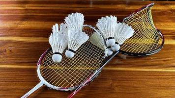 close-up de raquetes de badminton quebradas e galos de peteca de badminton branco sobre fundo de madeira marrom foto