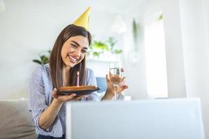 novo conceito normal. mulher feliz comemorando seu aniversário sozinha. jovem mulher segurando um bolo. festa de aniversário em casa. chamada de vídeo em família. distanciamento social. vida em casa. foto