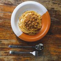 prato saudável de espaguete italiano coberto com um saboroso tomate e molho à bolonhesa de carne moída e manjericão fresco em uma mesa de madeira marrom rústica foto
