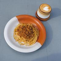 prato saudável de espaguete italiano coberto com um saboroso tomate e molho à bolonhesa de carne moída e manjericão fresco em uma mesa cinza. servido com capuccino foto