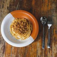 prato saudável de espaguete italiano coberto com um saboroso tomate e molho à bolonhesa de carne moída e manjericão fresco em uma mesa de madeira marrom rústica foto