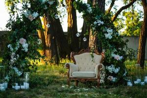 bela cerimônia de casamento ao ar livre. cadeiras decoradas ficam na grama. arco de casamento feito de pano e flores brancas e rosa em um fundo verde natural. portas antigas, estilo rústico. foto